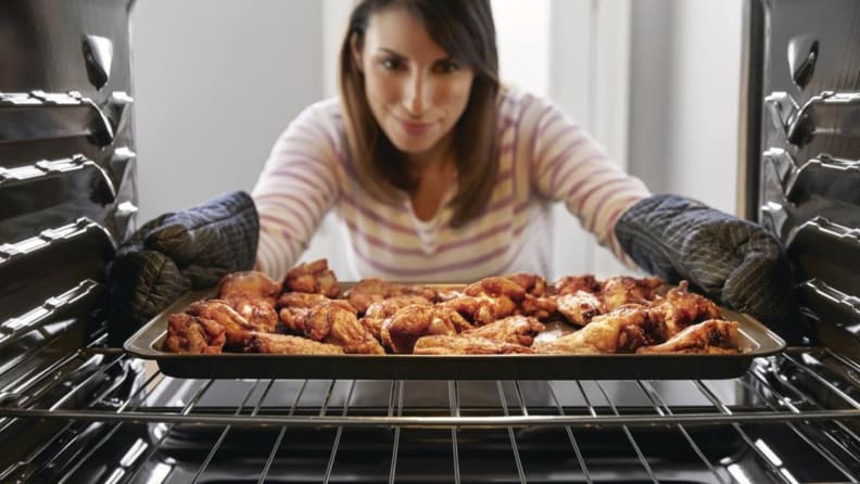 A person removes a tray of chicken wings from an oven.