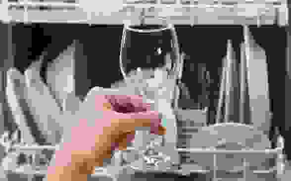 Someone examines a wine glass upon taking it out of the dishwasher.