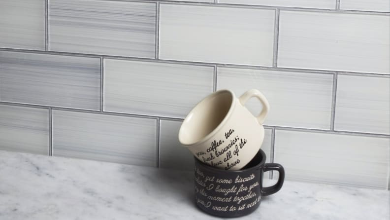 Two mugs stacked on top of each other against peel and stick tile, on top of marble countertop