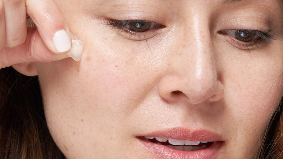 A woman taking a pimple patch off of her face.