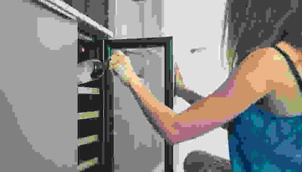 A woman pulls a bottle of wine out of a wine refrigerator.