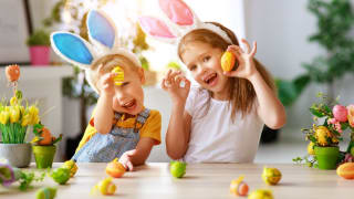 Brother and sister wearing bunny ears playfully hold up colored Easter eggs