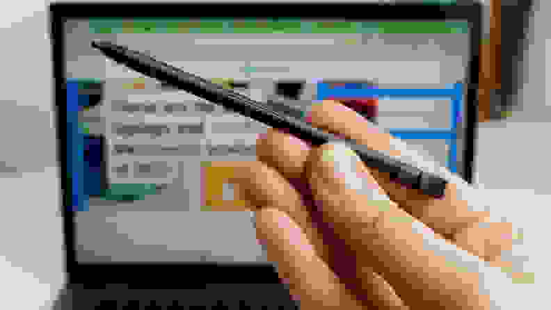 Person holding up stylus pen in front of the screen of the Lenovo ThinkPad L13 Yoga laptop.