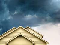 A close-up of the top of a tan-colored home with a tan roof next to an incoming tornado and dark skies
