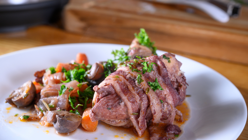 Plated coq au vin surrounded by vegetables on a white dish