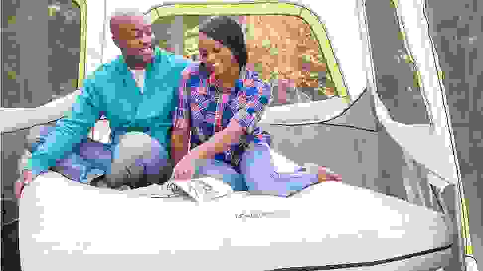 Couple sitting on a Coleman Camping Cot inside a tent reading a magazine