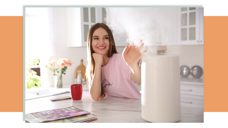 A person leaning against a counter and sticking their hand out toward a humidifier blowing mist out the top.