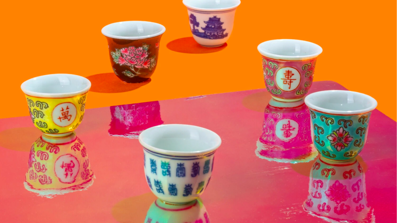 An image of several different handpainted wine cups in a variety of bright colors and patterns, on an orange and magenta background.