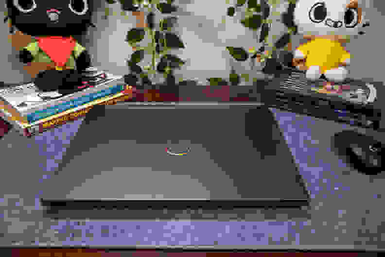 A black laptop, close, on top of a blue-gray mat flanked by books and plushies.