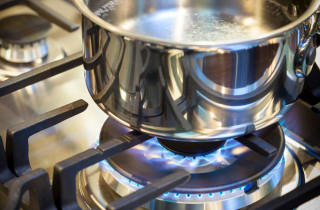 A pot of water sit on the burner of a gas stove with the flame on below it.
