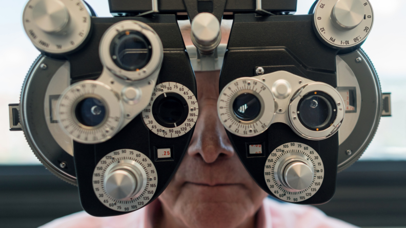 A senior patient looks through a device at an optometrist.