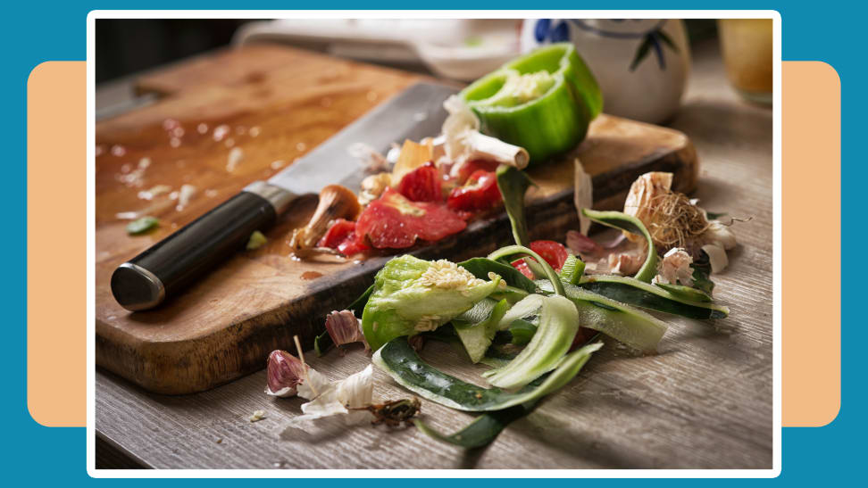 Vegetable scraps next to a wooden cutting board and knife on a blue and beige background