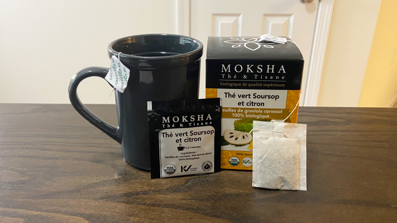 Table with a box of Moshka Soursoup Tea sitting on top next to a glass with a tea bag inside. Tea bags also sit outside the glass.