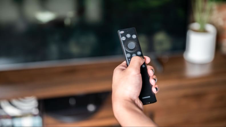 A hand holding the remote for the Samsung Q60B.