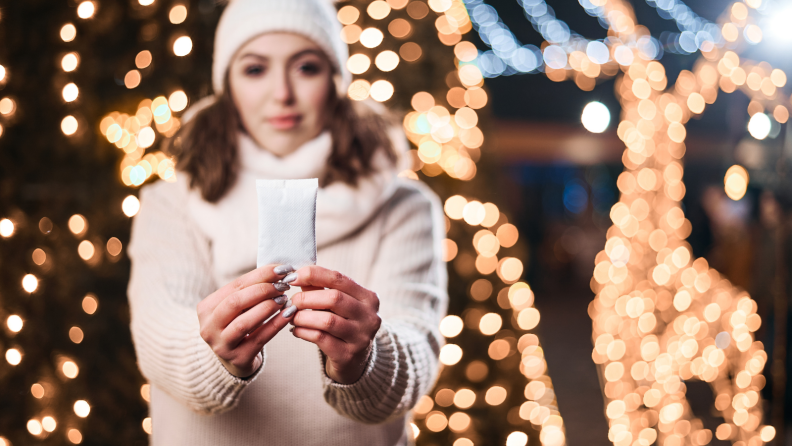 A person holding a hand warmer in front of outdoor twinkle lights.