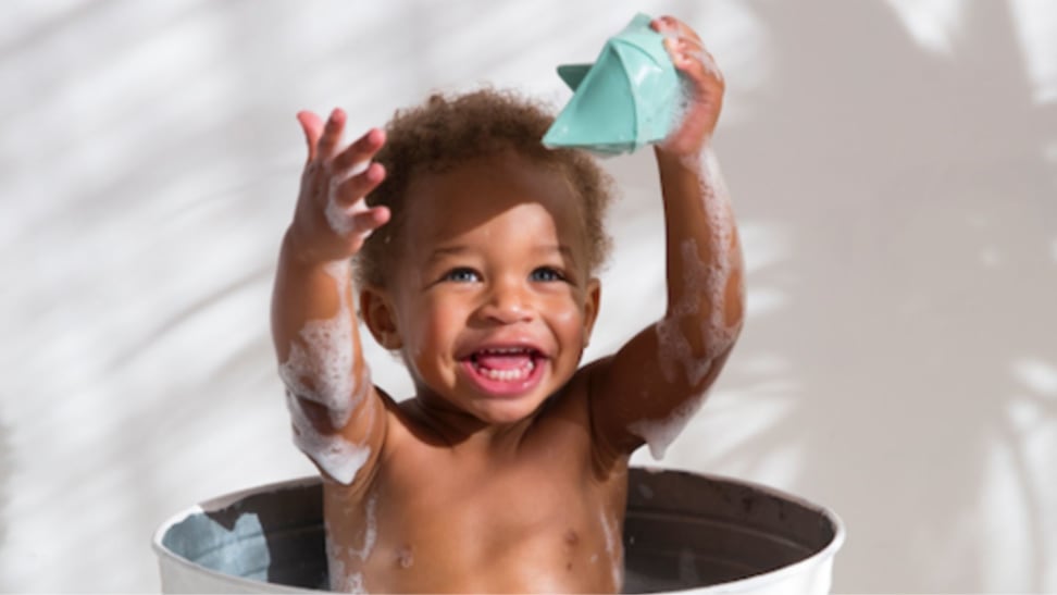 Toddler playing with a rubber origami boat in a bucket full of bath suds.