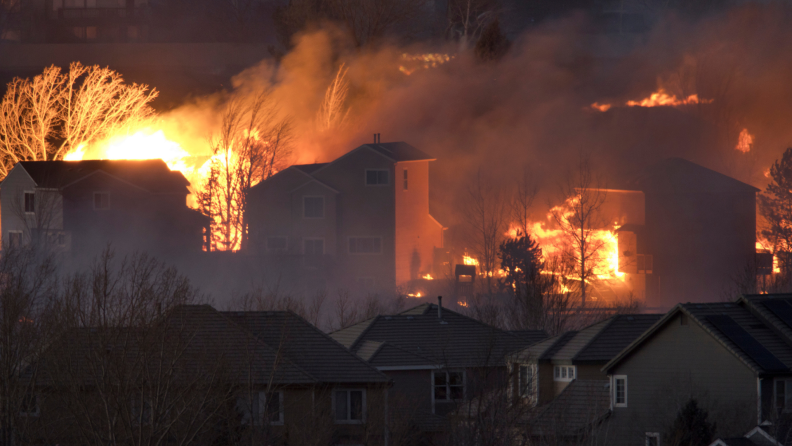 Wildfire spreading behind houses that are close proximity.