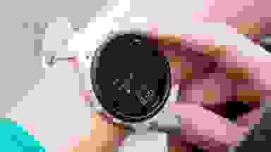 A woman holding a white, Garmin Forerunner 165 watch attached to her wrist.