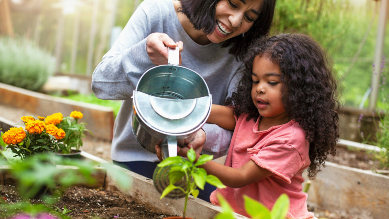 Mother helping daughter water garden with sprouts