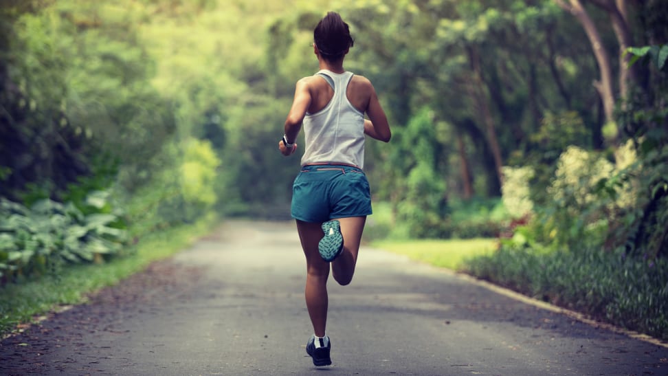 back of woman running in park wearing blue shorts and white tank top.