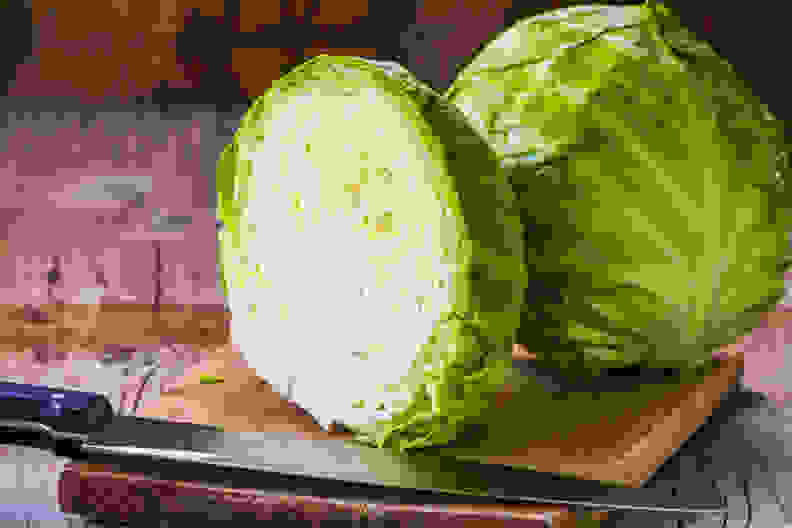 Fresh green cabbage cross section with water drops on rustic wooden cutting board, kitchen knife in forground. Close up, selective focus