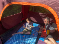 A child, a puppy, and a father recline in a Coleman Skylodge Instant Tent
