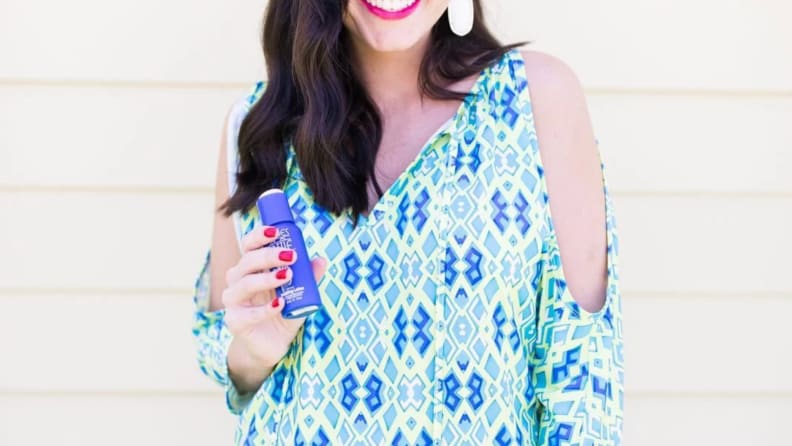 Person smiling while holding bottle of lotion.