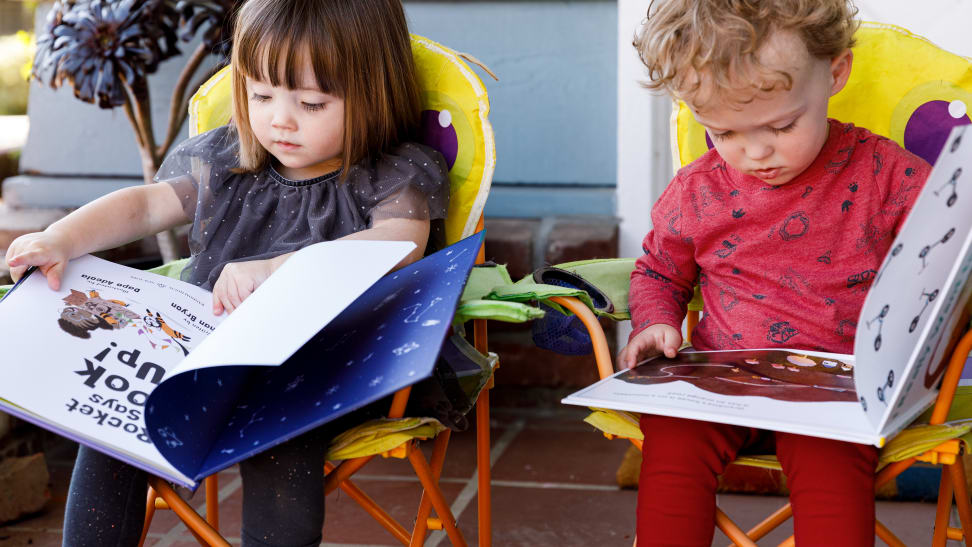 Two children read picture books outside.