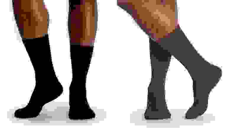 Pair of black socks from Bombas modeled on man's feet, pair of brown Bombas socks modeled on man's feet.
