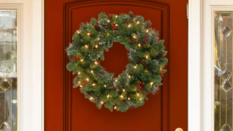 Artificial evergreen wreath with small string lights on a red door.