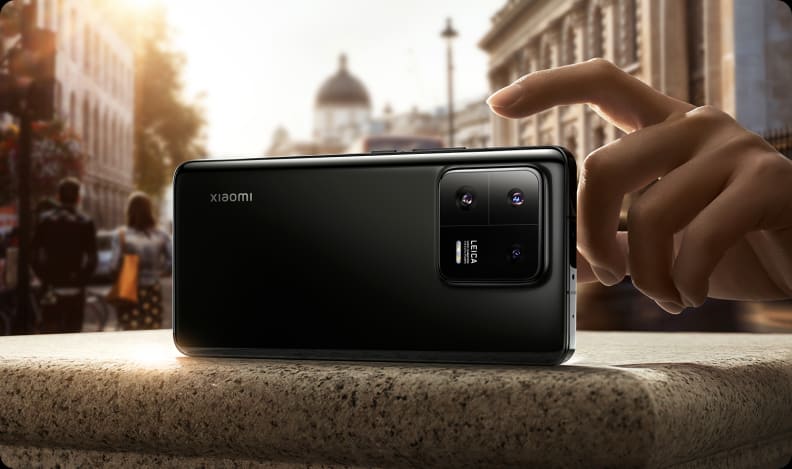 A Xiaomi 13 Pro smartphone in a cityscape sitting on a concrete surface with a hand about to take a photo.