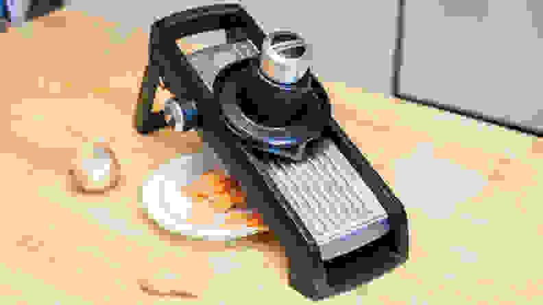 A KitchenAid mandoline sis on a kitchen counter with a plate of sliced sweet potatoes under it.