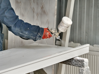 A person in protective clothing spraying white paint from a paint gun onto a piece of wood