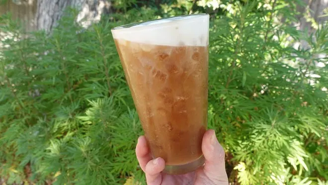 A person holds a glass with a cold brew coffee drink