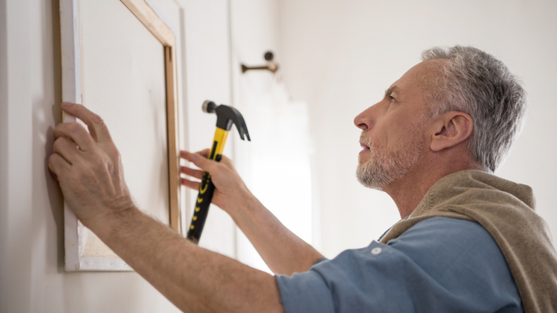 man hanging a framed picture on a wall