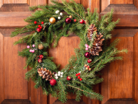 A wreath decorated with winter berries and pinecones against a natural wood door.