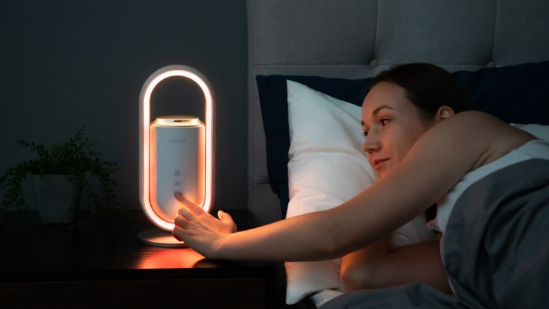 a woman in bed pushes a button on the aromeo sense