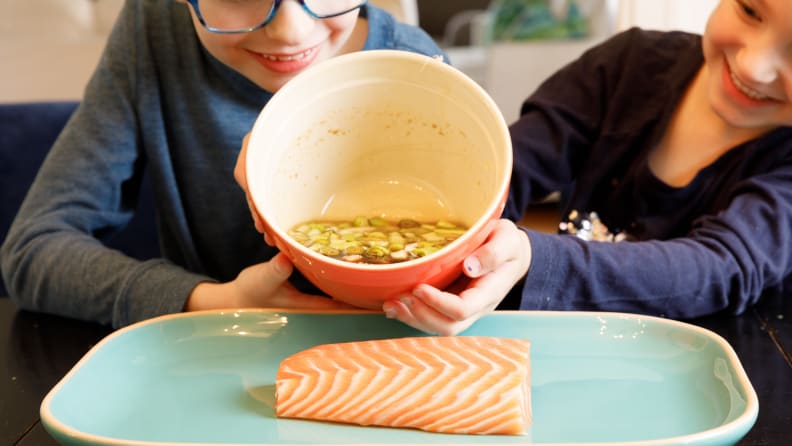 A boy and a girl pouring marinade on a piece of salmon