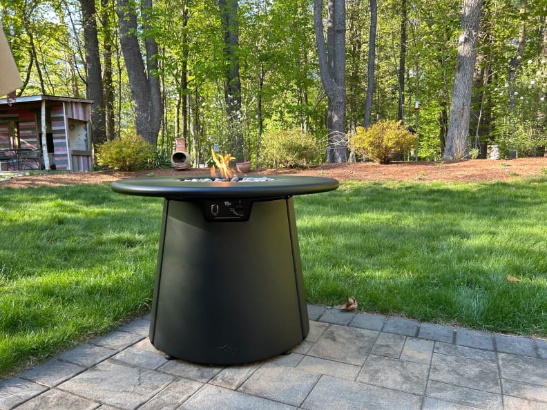 A black cylindrical fire pit sits on a patio outdoors with grass around