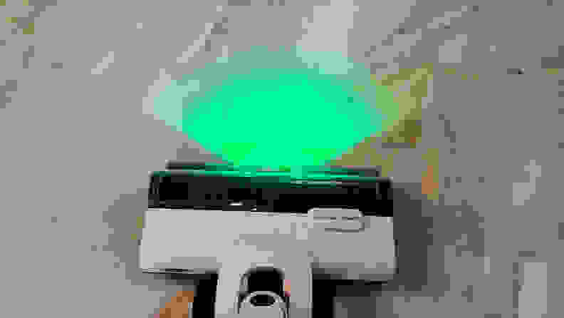 A white vacuum head shines a green light on a beige tile floor