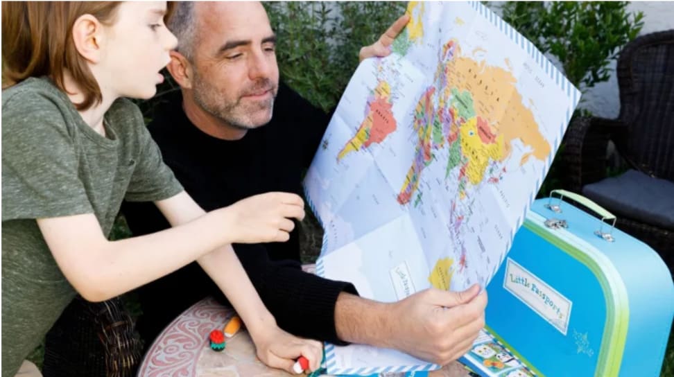 A child looks at a map with a bunch of international toys as he plays with a Little Passports box with his dad.