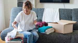 Person sorting folded clothes in order to donate them while sitting on couch.