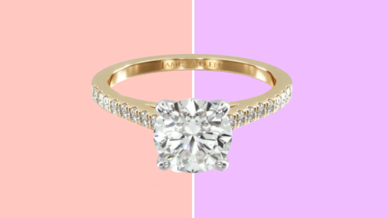 A gold diamond ring with a round diamond and paved side diamonds on the band.