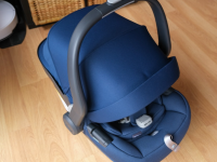 The Uppababy Mesa Max car seat in navy blue with hooded shade pulled all the way down on top of hardwood floor.