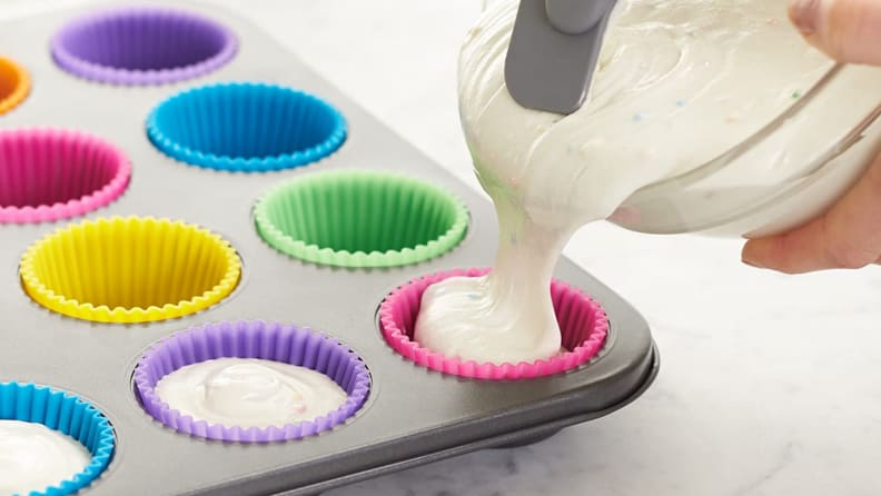A person pours cake batter into a muffin sheet.
