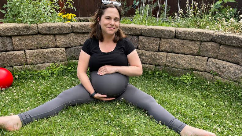 A pregnant woman sitting on the grass holding her belly and smiling