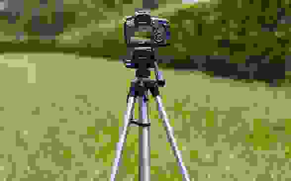 A tripod being used in a grass area to hold an iPhone that is taking photos.