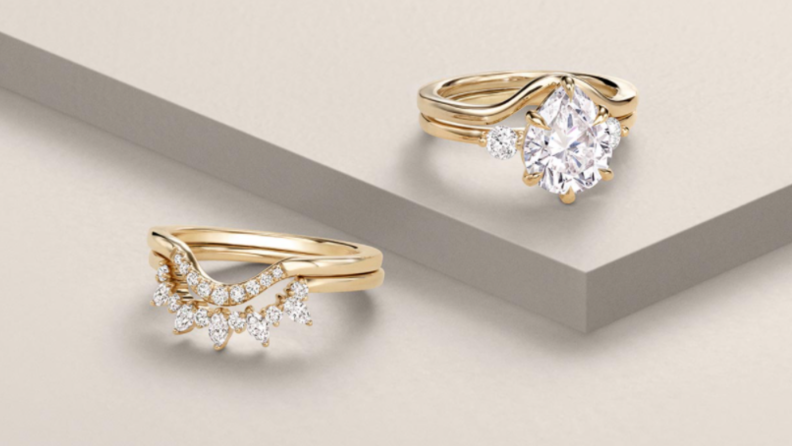 An image of two engagement rings from Brilliant Earth in gold settings, one with an attachable wedding band.