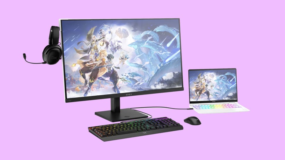The Omen Transcend gaming monitor in black connected to a white laptop, with a black keyboard in front of it and headphones floating to the left of it.