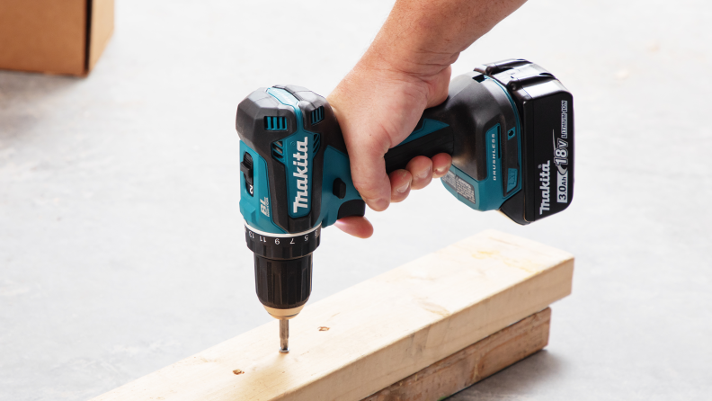 A hand holding the Makita Cordless Drill  that is being used to drill into wood